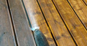 A close-up of a pressure washer cleaning a wooden deck with visible dirt and grime being removed.