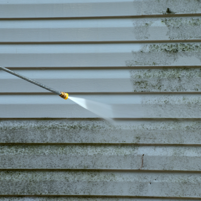 A close-up of wood cladding being cleaned with a power washer, removing dirt and grime.