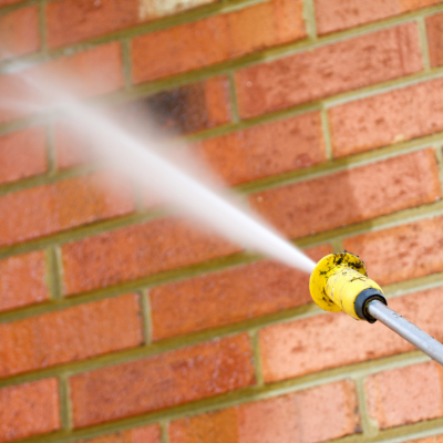 A yellow nozzle spraying pressure water on a red brick wall, cleaning off dirt and debris.