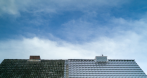 A roof with one half covered in moss and dirt, and the other half clean and pristine under a blue sky.