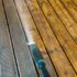 A close-up of a pressure washer cleaning a wooden deck with visible dirt and grime being removed.