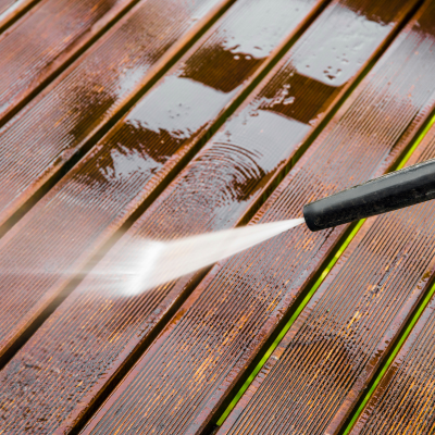 A high-pressure washer cleaning a wooden deck, removing dirt and stains from the grooves.