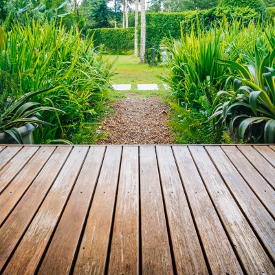 A clean wooden deck overlooking a lush green garden with hedges and a gravel pathway.