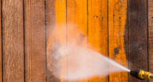 A pressure washer cleaning a weathered wooden fence, revealing a vibrant wood surface beneath.