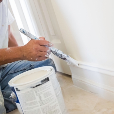 A painter applying light grey Elephant’s Breath paint to a skirting board with a fine brush.