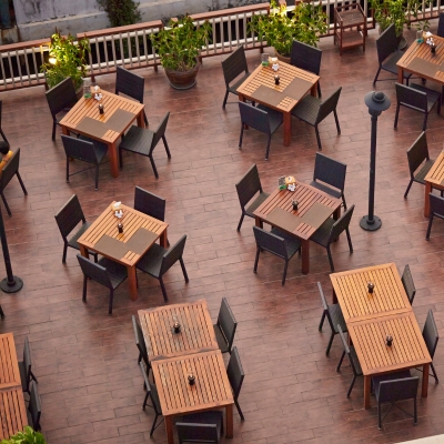 An outdoor restaurant with wooden decking, neatly arranged tables, and surrounding plants.