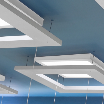 A suspended ceiling with rectangular white light fixtures hanging from a blue ceiling.