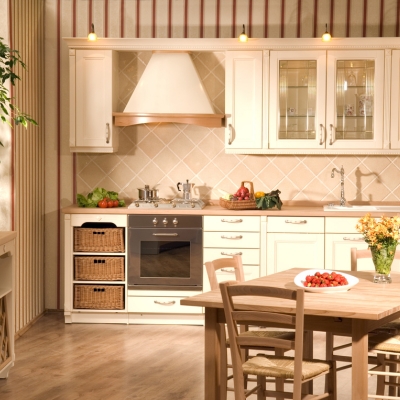 A traditional cream-coloured kitchen with wooden accents, wicker storage baskets, and a cosy dining area with warm lighting.