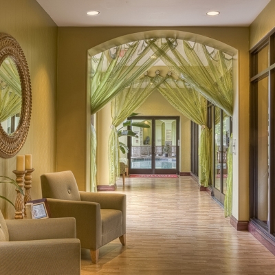 A spacious hallway painted in olive green, with elegant seating, soft lighting, and sheer green drapes.