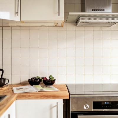 A kitchen backsplash with white square tiles, a wooden worktop, and a modern oven, demonstrating an easy tile refresh option.