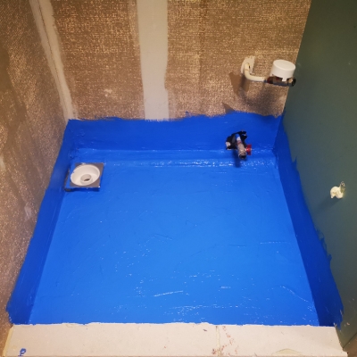 A wet room floor coated in bright blue waterproofing membrane with a central drain.