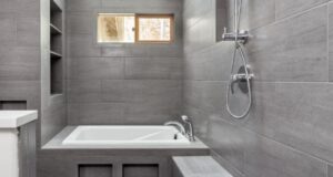 A modern wet room with grey tiles, a built-in bathtub, and a rainfall shower.