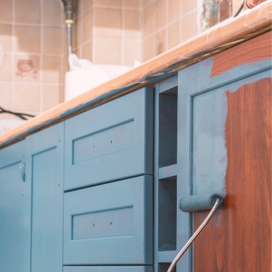 A modern kitchen with sage green cabinets, white worktops, and classic panelled doors, showing an updated look without full replacement.