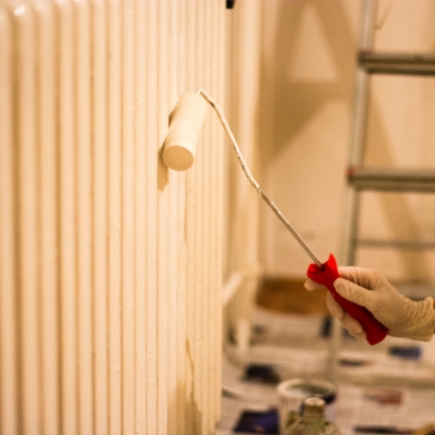 A person applying white radiator paint with a small roller for a smooth finish.